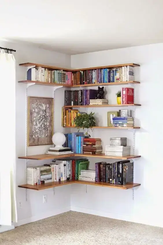 Estante de canto com prateleiras de madeira e livros variados Estante de canto com prateleiras de madeira e livros variados