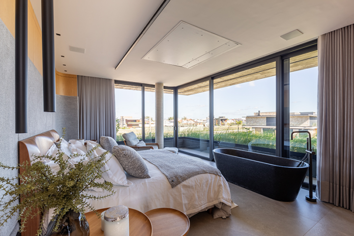 Projeto: Mayresse Arquitetura | A suíte master da Casa Terroir traduz o conceito de refúgio minimalista, com vista para a piscina, luz natural abundante e materiais quentes que criam uma atmosfera serena e contemplativa.