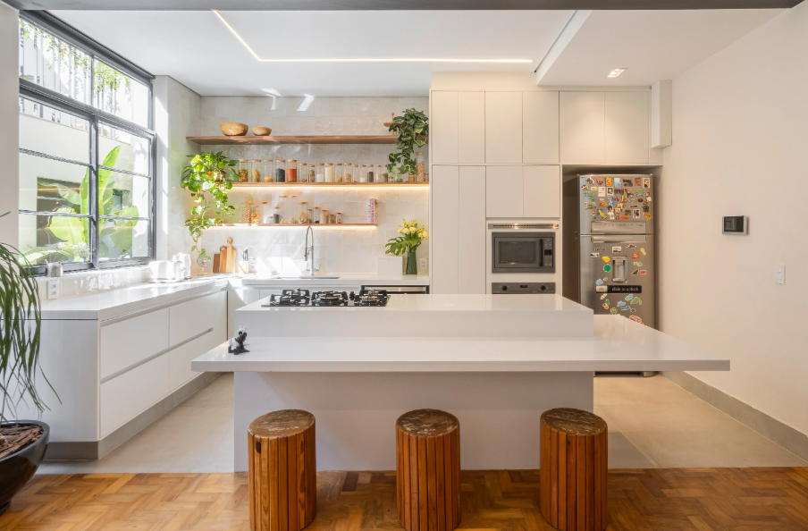 2. Cozinha em L com ilha central, cooktop na bancada e torre quente com forno e micro-ondas embutidos – Foto: Lucas Marco | Projeto: Debora Toledo Arquitetura